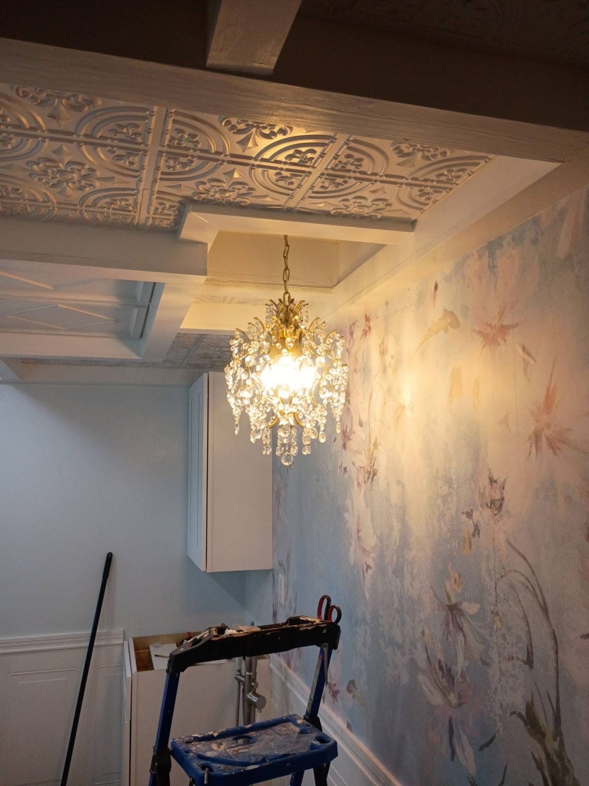Crystal chandelier hanging from the new coffered ceiling beside a floral mural wall