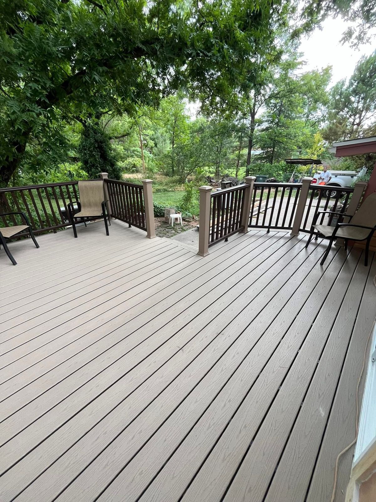 Finished composite deck surface with brown railings and patio chairs under shade trees