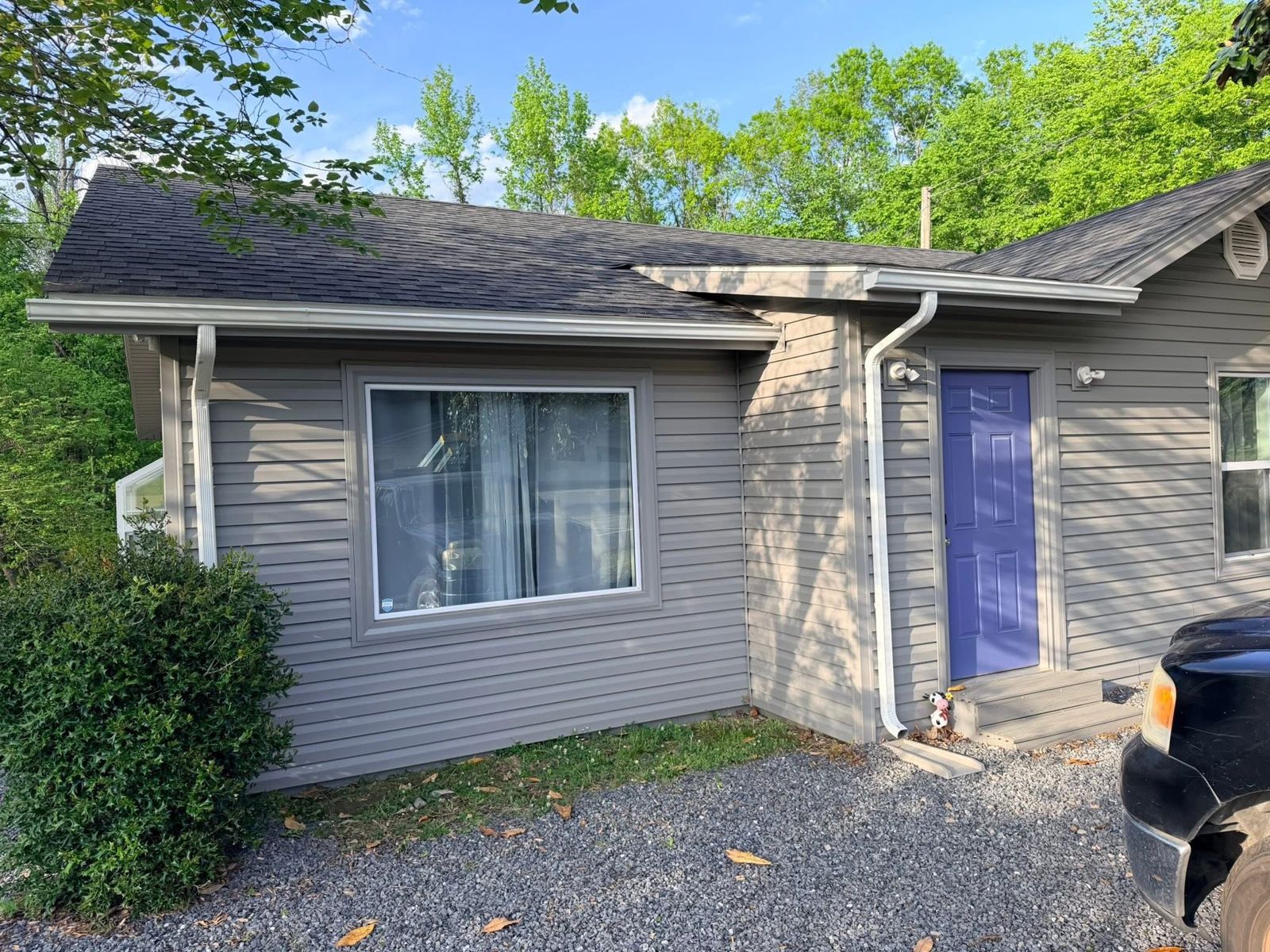 Front of a house with new white gutters and downspouts on gray vinyl siding and a purple front door