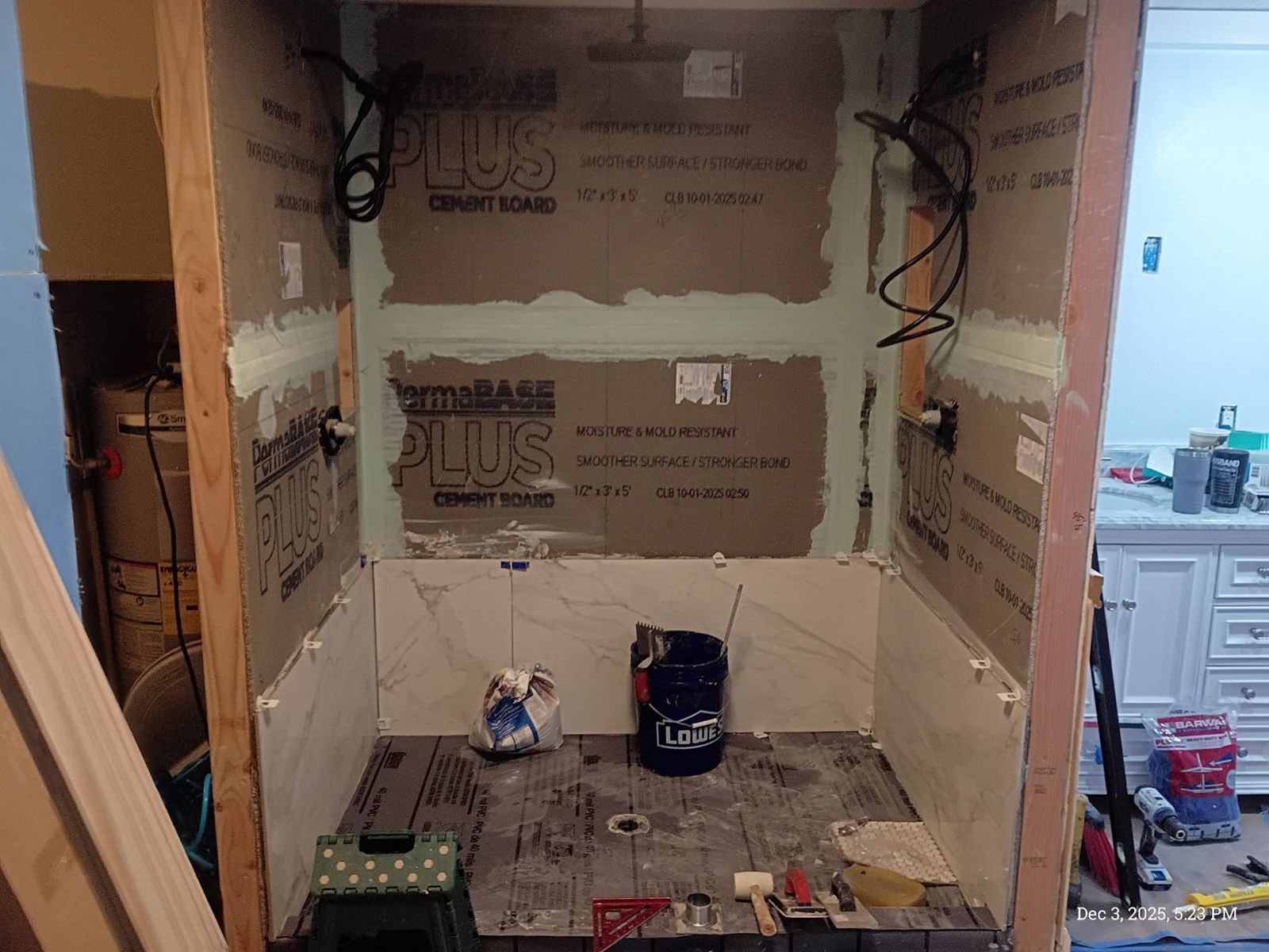 New shower framed and lined with moisture-resistant cement board, first row of marble-look tile going in